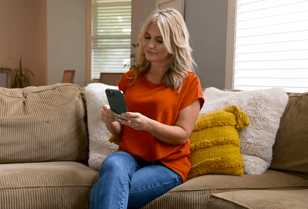 Photo of woman sitting on her couch using smartphone to sell their car using CarSolve.